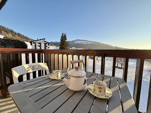 A wooden deck with a table set for tea, overlooking a snowy landscape with buildings and trees. - Cozy studio in Notre-Dame-de-Bellecombe near the slopes (Notre-Dame-de-Bellecombe)