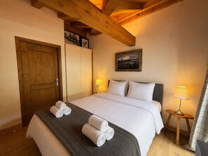 Un dormitorio con una cama, una puerta de madera, un armario, un cuadro, una lámpara y una ventana con cortinas.