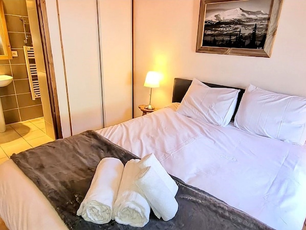 A hotel room with a bed, a nightstand with a lamp, a framed picture on the wall, and a towel on the bed.