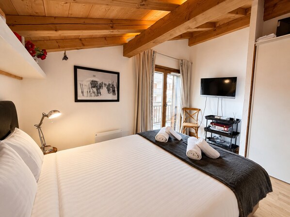 A hotel room with a bed, a desk with a TV, a chair, and a window with curtains.