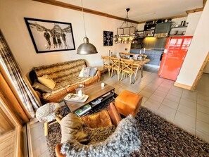 Un salon comprenant un canapé, une table basse et un tapis. On y trouve également une table à manger avec des chaises, ainsi qu’un coin cuisine équipé d’un réfrigérateur.