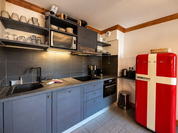 Una cocina moderna con armarios grises, un refrigerador rojo y blanco, y un microondas integrado.