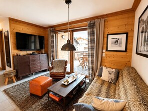 A cozy living room with a sofa, armchair, coffee table, and a television.
