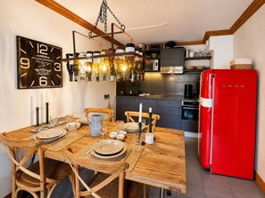 A dining area with a wooden table set for four, a red refrigerator, and a kitchen in the background.