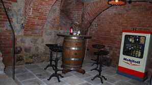 A bar area with a wooden barrel, two stools, a vintage-style lamp, and a Mobilioil branded refrigerator. - Alte Schmiede (Bad Griesbach im Rottal)