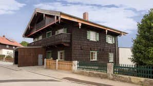 A two-story wooden house with a balcony, a small attached garage, and a green fence. - Alte Schmiede (Bad Griesbach im Rottal)