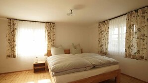 A bedroom with a wooden bed, floral curtains, a nightstand, and a ceiling fan. - Alte Schmiede (Bad Griesbach im Rottal)