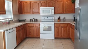 A modern kitchen with wooden cabinets, a white dishwasher, a double oven, a microwave, and a refrigerator. - Extra Spacious Florida Villa, 15 mins to Disney. (Davenport)