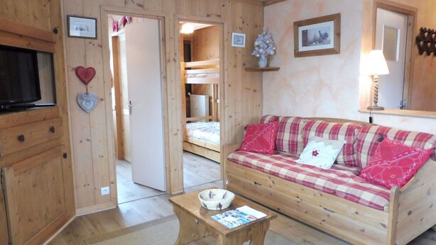 A cozy wooden room with a bunk bed, a sofa with plaid cushions, a small wooden table, and a television. - Cozy 2-Bedroom Apartment with Cabins in Crest-Voland - Near Slopes, Sleeps 6 (Crest-Voland)