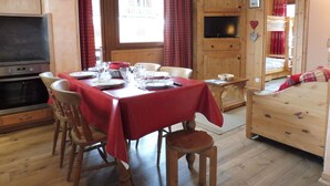 A cozy dining area with a wooden table set for four, a television, and a window with curtains. - Cozy 2-Bedroom Apartment with Cabins in Crest-Voland - Near Slopes, Sleeps 6 (Crest-Voland)
