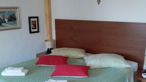 Una cama bien tendida con ropa de cama verde, almohadas rojas y blancas, y toallas blancas.