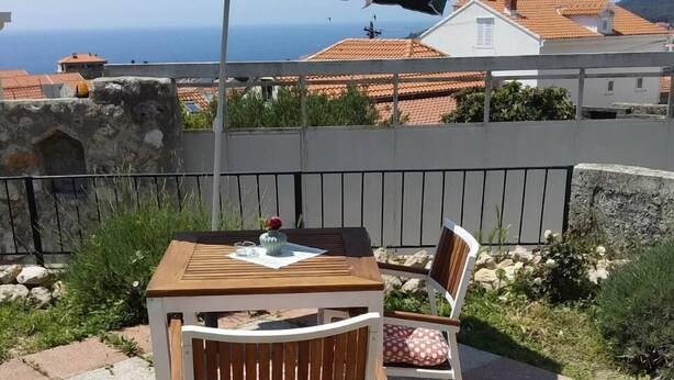 Un patio con una mesa de madera y dos sillas, una sombrilla verde y una planta en maceta.