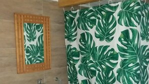 Un baño con lavamanos blanco, espejo y cortina de ducha con estampado de hojas verdes.