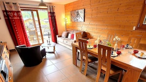 A dining area with a wooden table and chairs, a sofa, and a view of the outside. - Bright 2BR Apartment with Terrace and Parking, Sleeps 4, Les Gets (Les Gets)