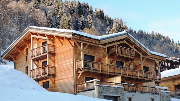 A multi-story wooden chalet with balconies, set against a snowy mountain backdrop. - Bright 2BR Apartment with Terrace and Parking, Sleeps 4, Les Gets (Les Gets)