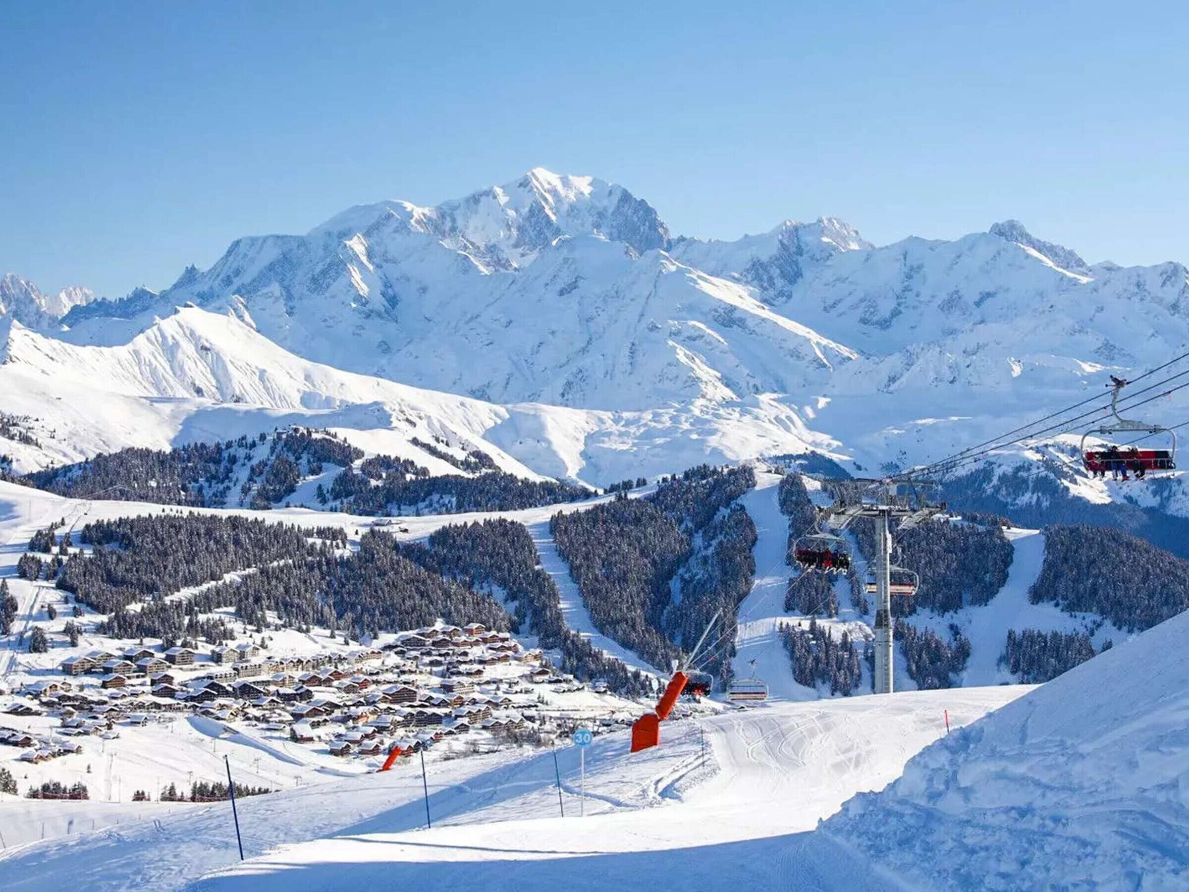 Eine verschneite Berglandschaft mit einer Seilbahn, einem Skigebiet mit Gebäuden und einem klaren Himmel.