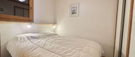 A bedroom with a bed, a window, a picture on the wall, and wooden beams on the ceiling.