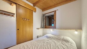 Un dormitorio con techo de madera, una cama con edredón blanco, una puerta de madera y una ventana con un espejo encima.