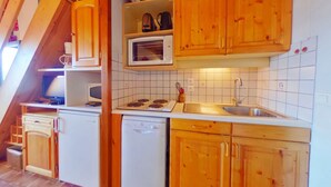 Una cocina compacta con armarios de madera, microondas, pileta y lavavajillas.