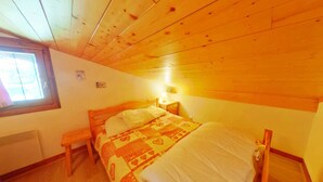 Un dormitorio con techo de madera, una cama individual, una mesita de noche con lámpara y una ventana.