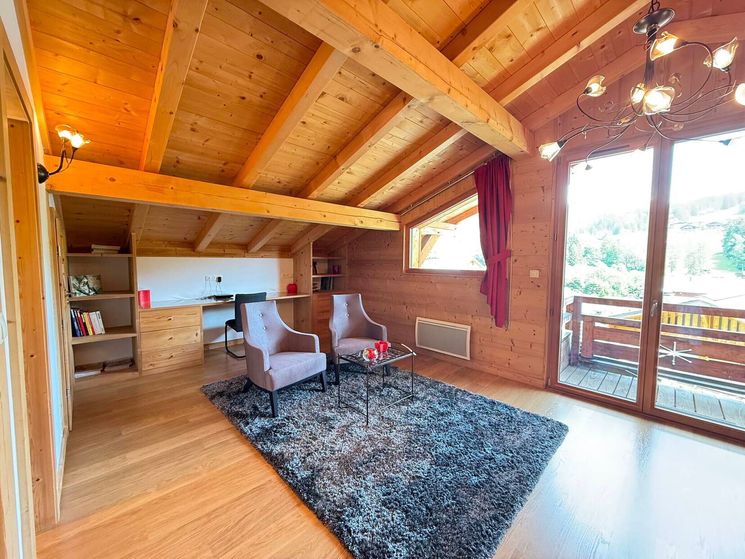 Un intérieur en bois comprenant un bureau, deux chaises, un tapis et une grande fenêtre donnant sur un paysage.