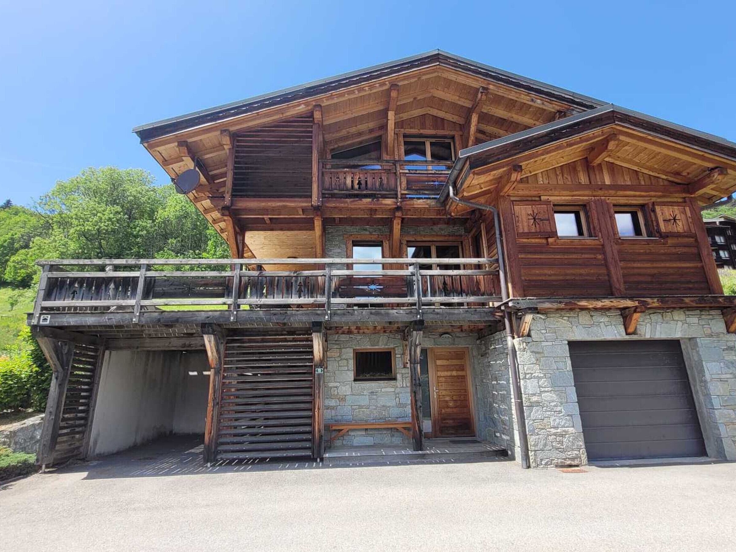 A multi-story wooden chalet with a balcony, stone foundation, and a garage.