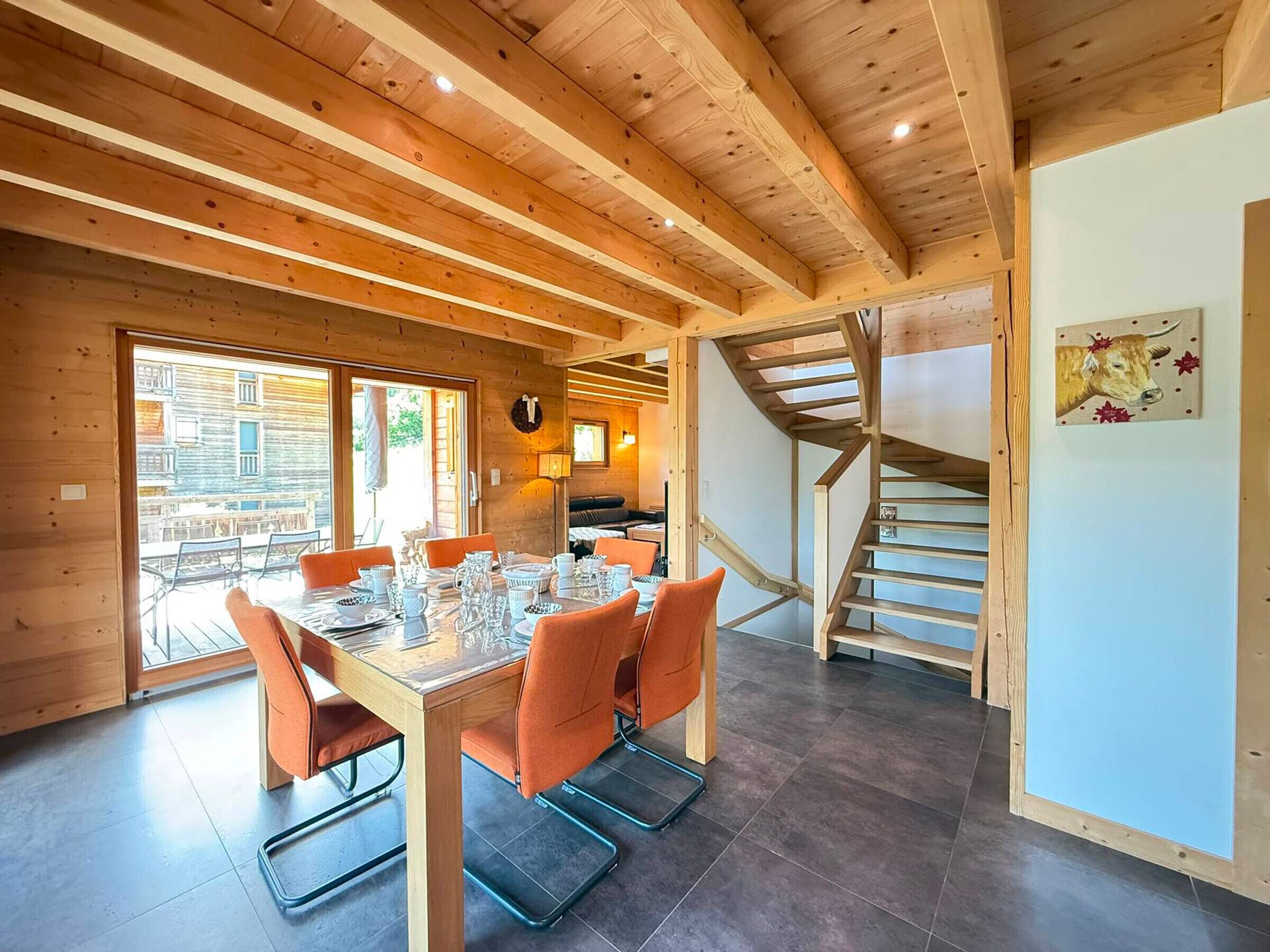 A wooden interior with a dining table, chairs, a staircase, and a view through a glass door.