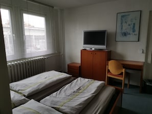 A bedroom with a bed, a desk, a chair, a radiator, and a television on a cabinet. - Pension am Messegelände (Magdeburg)