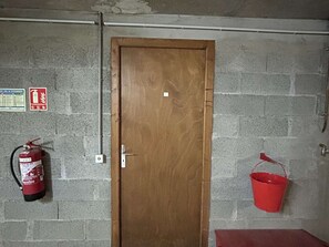 Une porte en bois dans une pièce où l’on aperçoit un extincteur et un seau rouge accroché au mur.