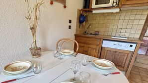 Une table à manger dressée avec des assiettes, des verres et des couverts, dans une cuisine dotée de meubles en bois et d’un lave-vaisselle Bosch.