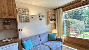 Un salon chaleureux avec un canapé gris, des meubles en bois et une grande fenêtre donnant sur le jardin.