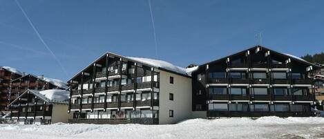 A large, multi-story building with balconies, likely a hotel or resort, surrounded by snow.