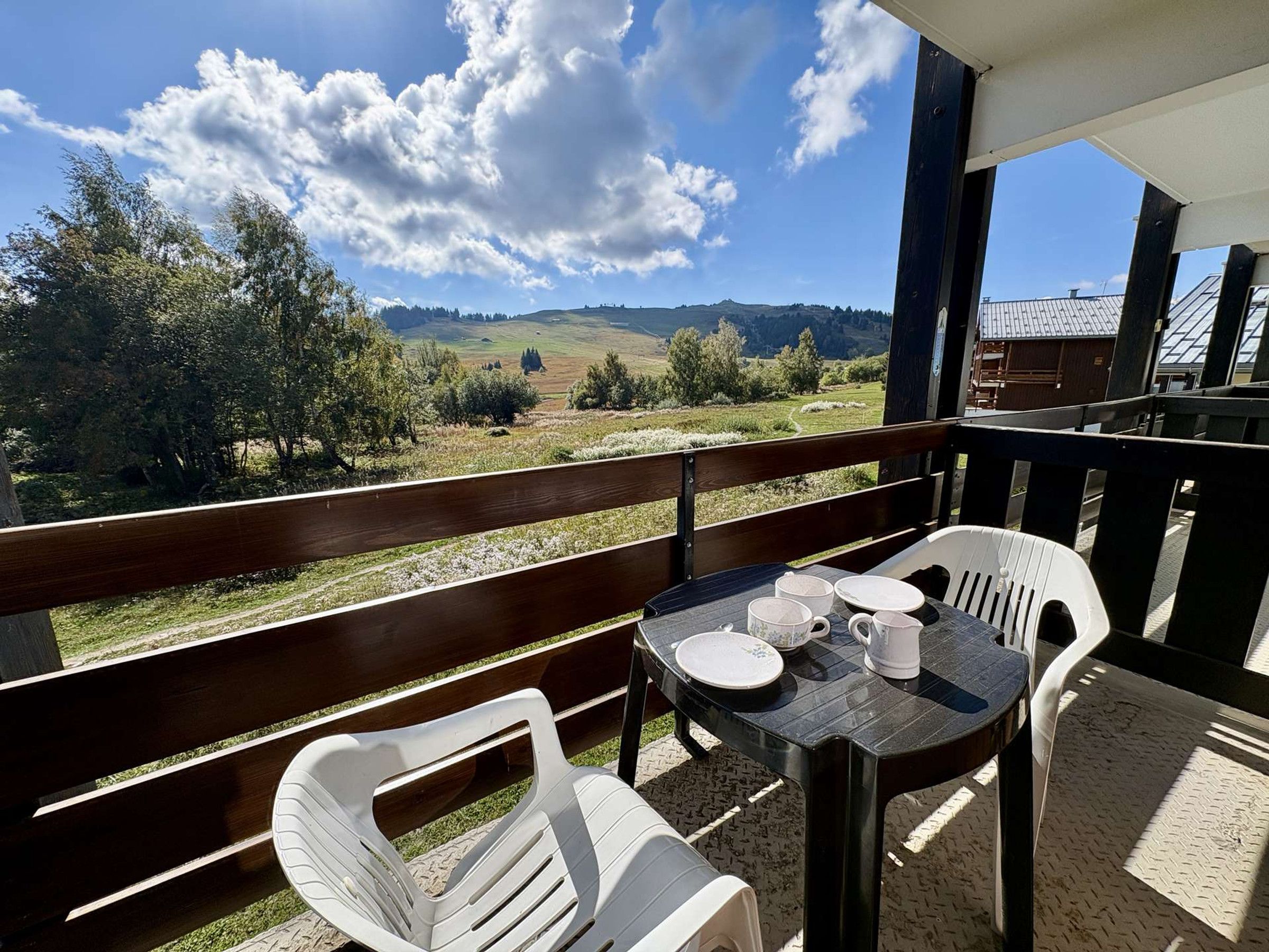 A balcony with a table and chairs, overlooking a rural landscape with hills and trees.