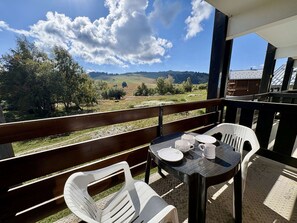 A balcony with a table and chairs, overlooking a rural landscape with hills and trees.