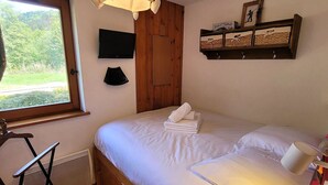 A bedroom with a bed, a television, a window, a shelf with decorative items, and a radiator.