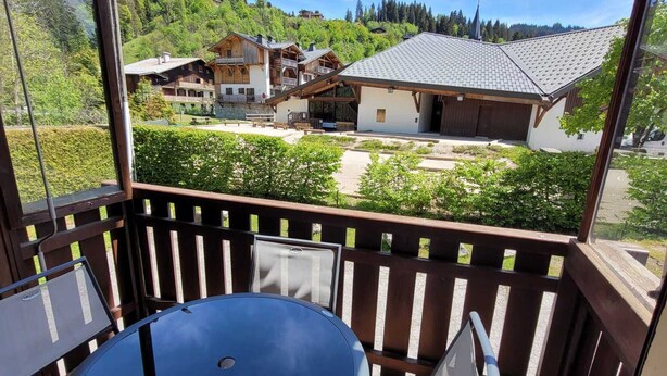 A balcony with a table and chairs, overlooking a village with traditional buildings and a church.
