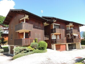 A two-story wooden building with balconies, a garage, and a small garden area.