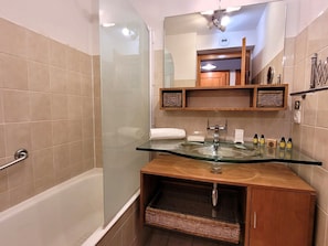 A bathroom with a glass-enclosed shower, a wooden vanity with a glass sink, and a mirror above the vanity.