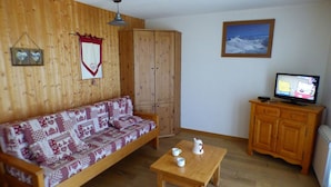 A cozy room with a wooden sofa, a small wooden table with cups, a television, and a wooden cabinet. - 3-room Apartment, 2 Bedrooms, 8 ppl, Les Saisies (Les Saisies)