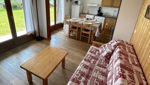A cozy living room with a wooden table and sofa, a dining area with a table set for four, and a kitchen with basic appliances. - 3-room Apartment, 2 Bedrooms, 8 ppl, Les Saisies (Les Saisies)