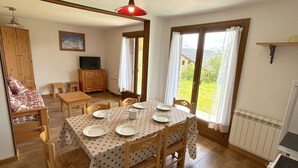 A dining area with a table set for four, wooden chairs, a television, and a view of the outdoors through large windows. - 3-room Apartment, 2 Bedrooms, 8 ppl, Les Saisies (Les Saisies)