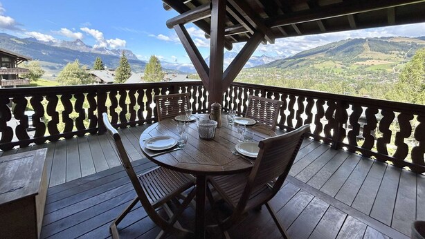 A wooden deck with a table set for dining, overlooking a mountainous landscape.