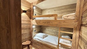 A bunk bed room with wooden walls and a small stool.