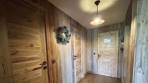 A hallway with wooden walls and doors, a hanging light fixture, and a wreath on one door.