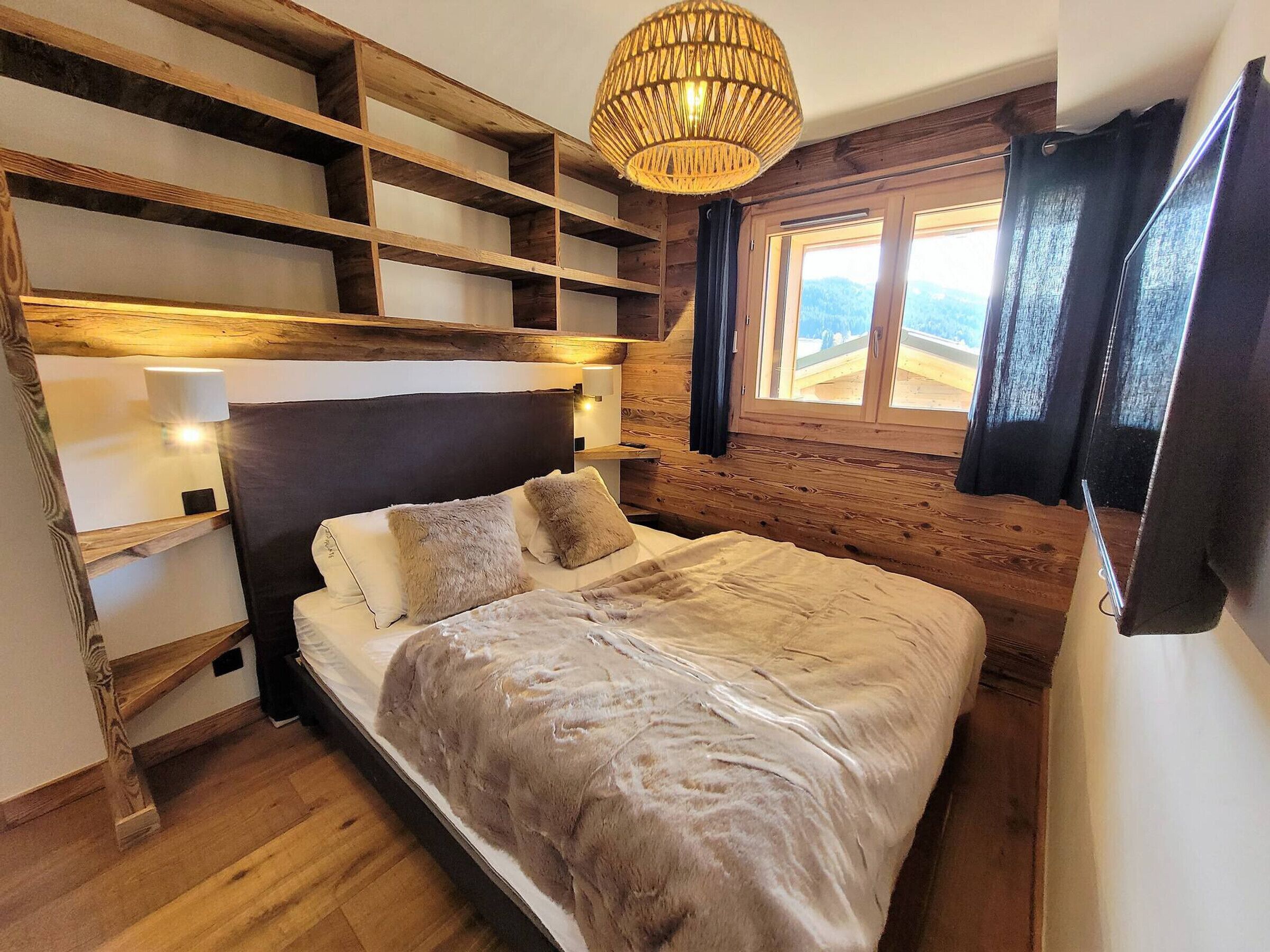 A cozy bedroom with a wooden headboard, a large bed with a fluffy blanket, and a window with curtains.