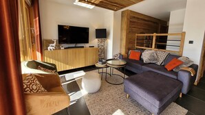 A modern living room with a wooden ceiling, a flat-screen TV, a sofa set, and a coffee table.
