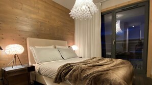 A modern bedroom with a wooden headboard, a large bed with a fluffy blanket, two bedside lamps, and a chandelier.