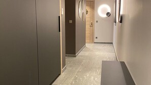 A narrow hallway with a modern design, featuring a light fixture on the wall and a door at the end.