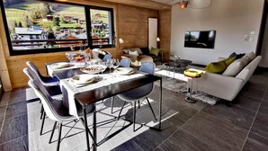 A modern dining area with a wooden table set for four, a sofa, and a TV in a living area.