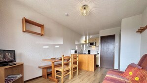 A compact living space with a wooden dining table, a sofa, a TV, and a kitchenette. - Cozy Studio in Notre-Dame-de-Bellecombe - Ski-in/Ski-out, Sleeps 4, Parking & Balcony (Notre-Dame-de-Bellecombe)